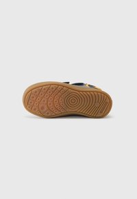 Sneakers Geox mają teksturowaną gumową podeszwę z okrągłymi wzorami, brązowy kolor oraz granatową cholewkę uzupełnioną żółtymi akcentami.