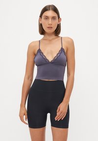 Paarse bralette met kantafwerking en dunne bandjes, gecombineerd met hoge zwarte shorts. Glad materiaal met een aansluitend ontwerp.