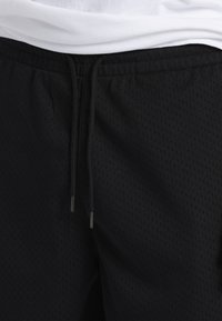 Shorts sportivi neri realizzati in tessuto a rete traspirante, con vita regolabile tramite cordino e piccole aperture di ventilazione sulla superficie.