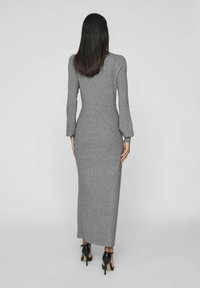 Abito lungo grigio a maglia, aderente, con maniche lunghe e polsini a campana. Il tessuto è morbido, con un collo alto e un design lungo fino al pavimento.
