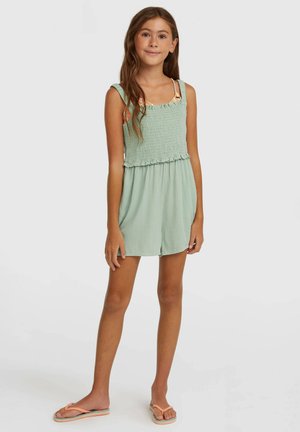 Mono corto verde menta con cuerpo fruncido, borde con volantes en la cintura y tirantes delgados. Se lleva con chanclas rosa claro, con tela texturizada.