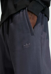 M�ørkegrå atletikbukser lavet af blødt stof, med et lille broderet logo og sidelommer med diskrete teksturdetaljer.