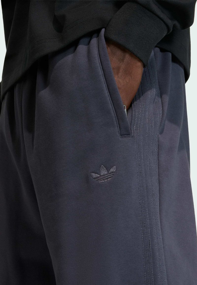 Mørkegrå atletikbukser lavet af blødt stof, med et lille broderet logo og sidelommer med diskrete teksturdetaljer.