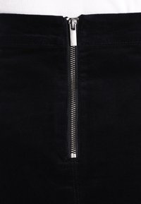 Musta corduroy-hame, jossa on keskilinjassa metallivetoketju ja tekstuuri, tasainen pinta ja pystysuora raidoitus kauttaaltaan.