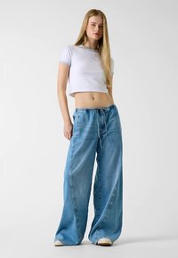 White cropped t-shirt with light blue trim, paired with wide-leg light blue denim pants featuring an elastic waistband and drawstring.