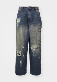 Jeans azules de talle alto con parches desgastados, un degradado y tachuelas decorativas a lo largo de un lado, con un ajuste suelto y de pierna ancha.