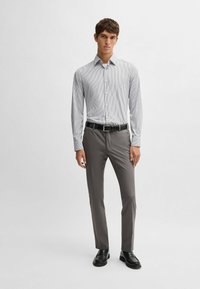 Chemise rayée à manches longues blanche et grise, associée à un pantalon gris et des chaussures noires. Présente un col classique et une fermeture à boutons.