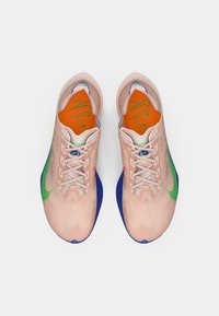 Pár rózsaszín sportcipő zöld swoosh-sal, kék középtalpakkal és narancssárga talpbetétekkel, zöld logókkal, felülnézetből.