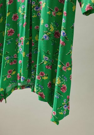 Blomstret kjole i grøn stof med lyse pink, gule og blå blomster, afslappet pasform og en buet kant.