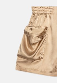 Short en tissu satin avec une taille smockée, comprenant une poche latérale. La couleur est beige clair avec une texture lisse et brillante.