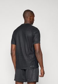 T-shirt de sport noir à manches courtes, avec un design texturé et un motif à carreaux subtil. Inclut une technologie de tissu anti-humidité.