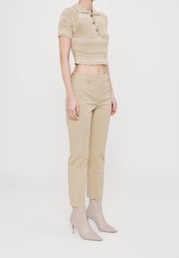 Polo top in maglia beige cropped con maniche corte e patta frontale, abbinato a pantaloni beige sartoriali e stivaletti beige con punta.
