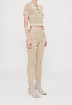 Beige cropped strik polo top med korte ærmer og en frontknaplukning, parret med beige skræddersyede bukser og spidse beige ankelstøvler.