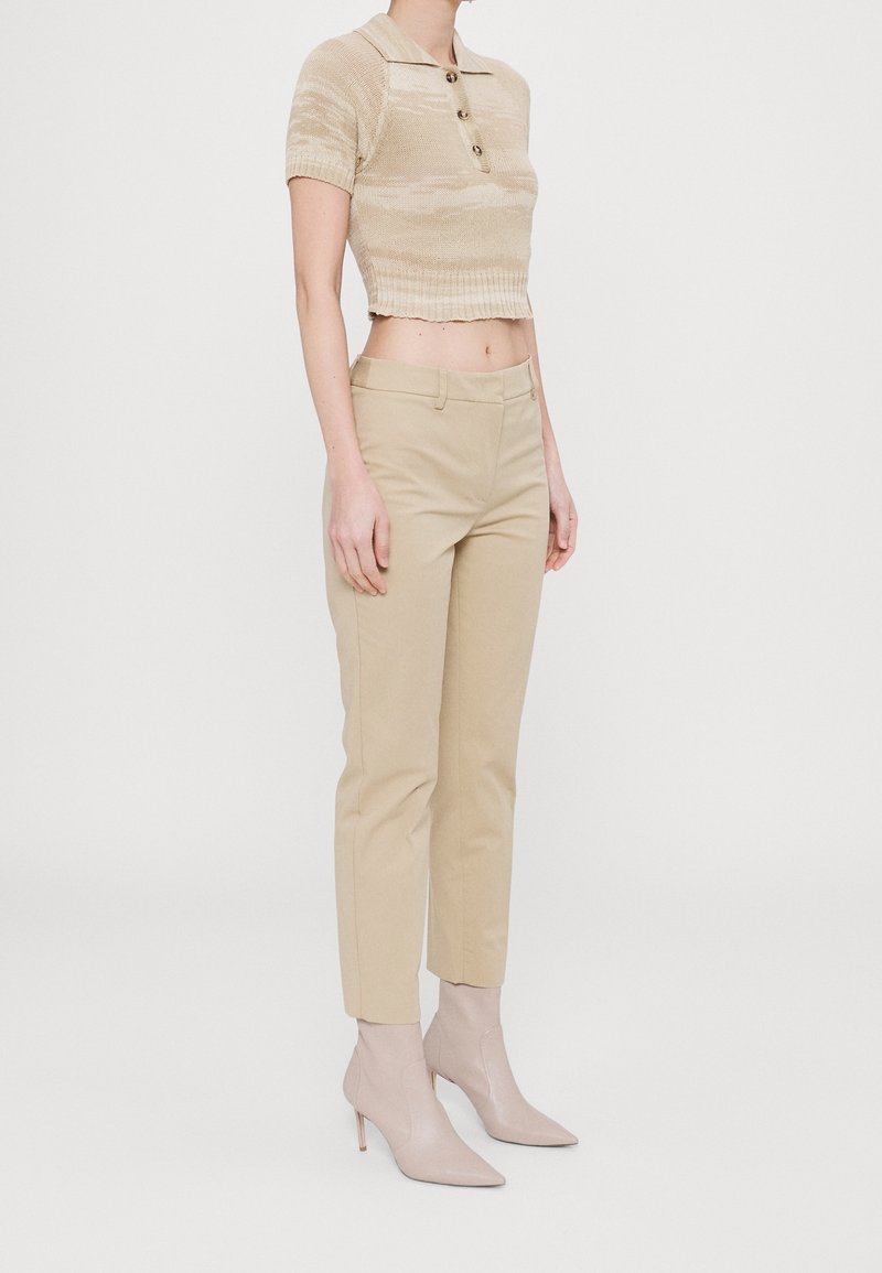 Polo top in maglia beige cropped con maniche corte e patta frontale, abbinato a pantaloni beige sartoriali e stivaletti beige con punta.