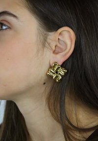 Złote kolczyki w kształcie kwiatów o bulwiastym kształcie, z gładkimi metalicznymi powierzchniami i teksturowanym środkiem, prezentowane na neutralnym tle.