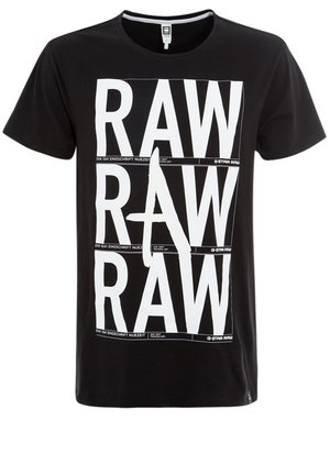 T-shirt noir à manches courtes avec un grand texte blanc en gras « RAW » imprimé trois fois verticalement sur le devant, avec une lettre A stylisée au centre.