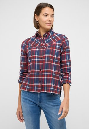Red, navy, and white plaid button-up shirt with a collar and rolled sleeves. Made of woven fabric, featuring a relaxed fit and side slits.