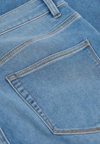 Close-up of blue denim fabric showing back pocket with orange stitching and a belt loop on a pair of jeans.