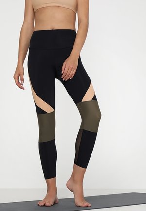 Sorte og beige atletiske leggings med udsnit; grønne accenter på underbenene; strækbart, tætsiddende materiale; mesh-paneler for åndbarhed.