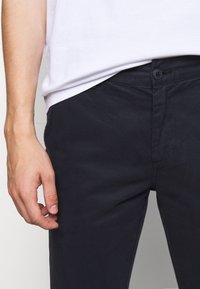Navy katoenen broeken met een slim fit. Voorzien van een knoopsluiting en zijzakken. De stof heeft een gladde textuur en minimale stikseldetails.