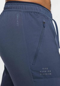 Męskie granatowe szorty do biegania wykonane z materiału Dri-FIT, z elastycznym pasem, boczną kieszenią na zamek oraz złotym logo Nike Running Division.