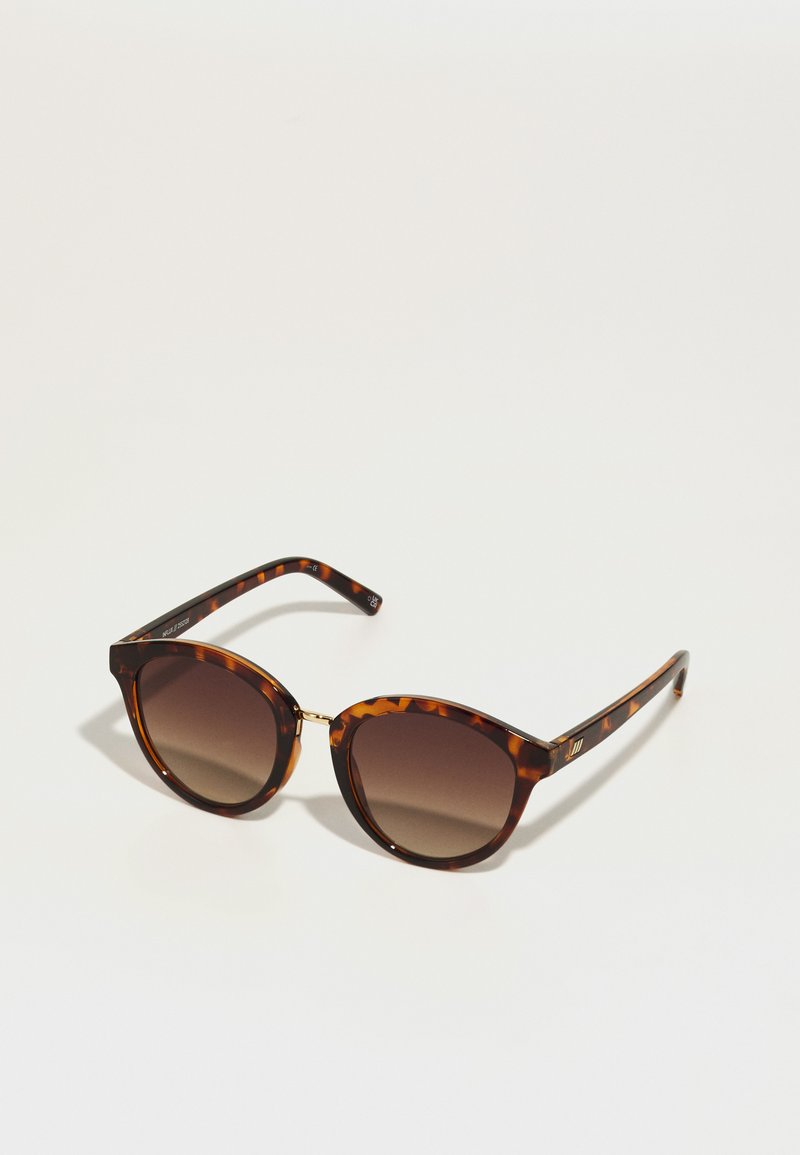 Ochelari de soare cu rame în stil țestoasă, lentile maro cu gradient. Formă de ochi de pisică, accent auriu lângă balama, brațe negre elegante cu detalii decorative.