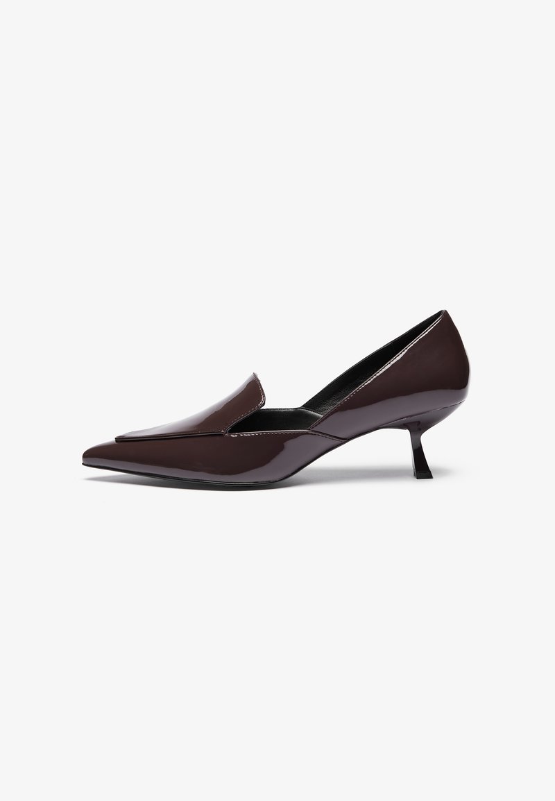 Korkeakorkoiset tummanruskeat patenttinit jalat, joissa on matala stiletto-korko ja sulava siluetti, jossa on hieman kohotettu varvasosa.