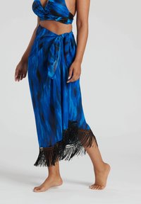 Blå sarong med knytmidja, med en gradientmönster och svart fransdetalj vid fållen. Tillverkad av lättviktsmaterial.