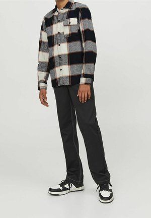 Geruite flanellen shirt in marineblauw, grijs en crème met oranje accenten, met een knoopsluiting en één borstzak. Gepaard met zwarte broek.