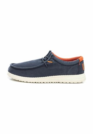 Zapato slip-on de lona azul marino con suela de goma blanca, interior naranja y un detalle decorativo de cordones en la parte superior.