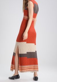 Stickad maxikjol i orange och kräm med grå detaljer, med en sidöppning och horisontellt randmönster vid fållen; ärmlös design.