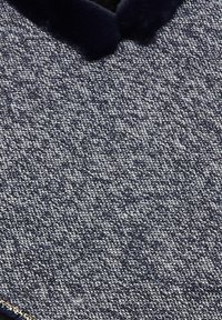 Tessuto navy a trama con un motivo intrecciato, dotato di un morbido colletto in pelliccia sintetica. Il design è strutturato con un collo rotondo e cuciture dettagliate.