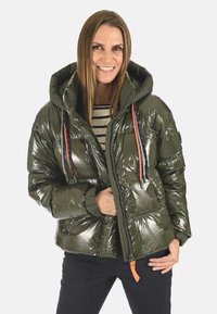 Veste rembourrée vert olive avec une finition brillante, capuche, cordons de serrage rouges, fermeture éclair et poche avant. Stylisée avec un design matelassé horizontal.
