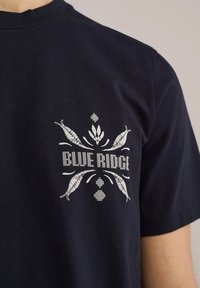 Sötétkék pamut póló, fehér grafikai mintákkal és középen a "BLUE RIDGE" felirattal.