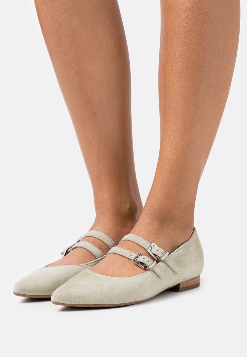 Ballerines en suède vert clair avec un bout pointu, deux brides à la cheville avec des boucles, et un petit talon en bois. Texture lisse avec un minimum de détails.