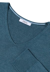 Teal v-hals trui met lange mouwen, met een geribde zak en halslijn. Gemaakt van zachte stof met een gladde textuur. Merktag zichtbaar.
