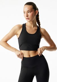 Sort atletisk crop-top med rund hals og tætsiddende design, kombineret med højtaljede sorte leggings med diskrete syninger og lommer.