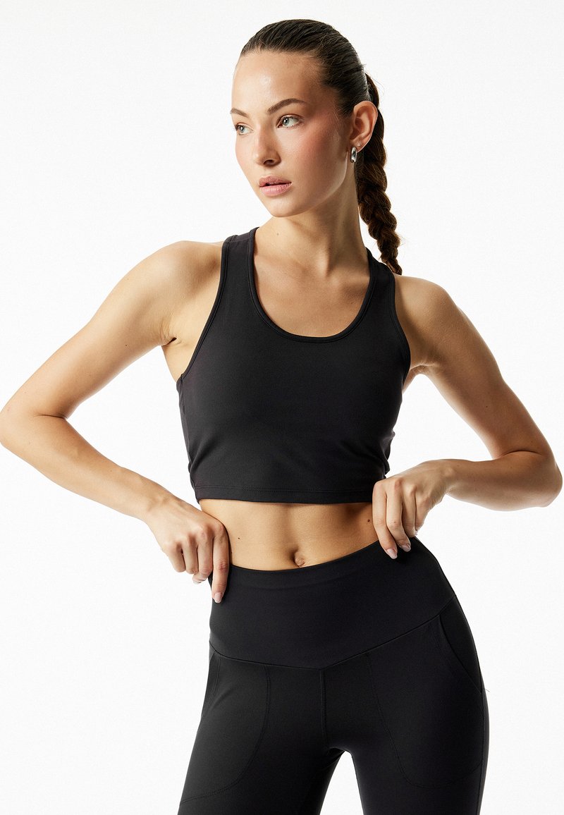 Sort atletisk crop-top med rund hals og tætsiddende design, kombineret med højtaljede sorte leggings med diskrete syninger og lommer.