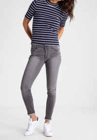 Niebiesko-białe paski, krótki rękaw w połączeniu z wyblakłymi szarymi obcisłymi dżinsami z przetarciem na kolanie, noszone z białymi trampkami.