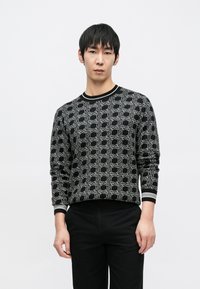 Juodas megztinis iš mezginio su geometriniu baltu raštu, ribotu apykakle ir rankogaliais, ilgomis rankovėmis ir aptemptu siluetu.