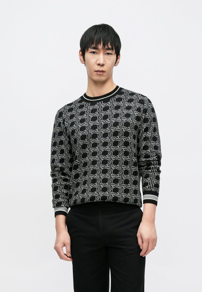 Juodas megztinis iš mezginio su geometriniu baltu raštu, ribotu apykakle ir rankogaliais, ilgomis rankovėmis ir aptemptu siluetu.