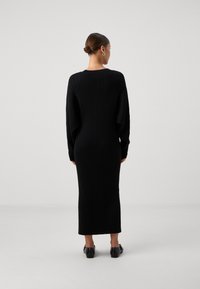 Črna rebrasta dolga obleka z ohlapnim prilegom. Ima okroglo ovratnico in sega do sredine meč, v kombinaciji s črnimi čevlji na blok peto.