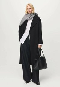 Zwarte wollen overjas, wit overhemd met knopen, antracietkleurige sjaal, brede donkere jeans en een zwarte handtas. Soepele texturen, minimalistisch ontwerp.