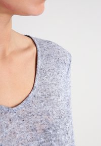 Hellgrauer Pullover mit lockerem, strukturiertem Strick, featuring einem weiten Rundhalsausschnitt und kurzen Ärmeln, der ein weiches, atmungsaktives Material betont.