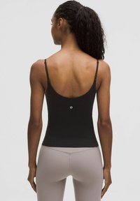Black fitted tank top with spaghetti straps, smooth texture, low back design, featuring a small logo at the center back. Paired with light leggings.
