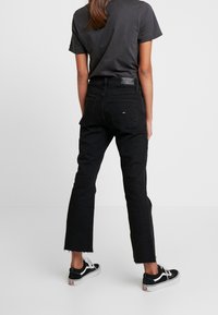 Černé džíny s krátkým rozšířeným designem a třepeným lemem, spárované s černo-bílými teniskami. Vidět je také šedé tričko.