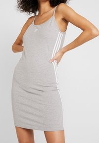 Szara sukienka bez rękawów wykonana z bawełny o dopasowanym kroju. Posiada białe pionowe paski wzdłuż boków oraz małe logo na piersi.