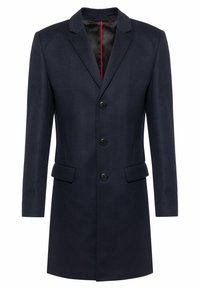 Abrigo azul marino de mezcla de lana con silueta ceñida, diseño de un solo pecho, tres botones delanteros y dos bolsillos laterales. Forro interior rojo.