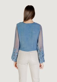 Top azul claro con mangas transparentes adornadas con intrincados bordados azules y lentejuelas. La parte trasera presenta un escote redondeado.