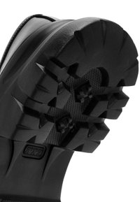 Zwarte laarzenzool met diepe profielpatronen, met verhoogde hoekige vormen, textuurgebieden voor grip en robuust, duurzaam rubbermateriaal.